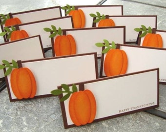 May include: A set of ten place cards with a brown border and a white background. Each card features a paper pumpkin with a green stem and leaves. The text "Happy Thanksgiving" is printed on one of the cards.