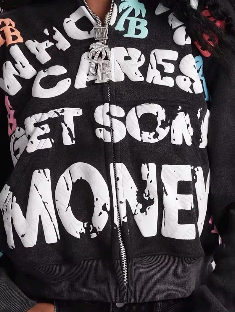 Op de afbeelding: Een donkergrijze hoodie met ritssluiting met de woorden "WHO CARES GET SOME MONEY" in grote witte letters. De hoodie heeft een distressed look en een zilveren rits. Een zilveren hanger met een palmboom en de letter "B" hangt aan de rits.