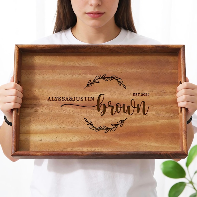 May include: A rectangular wooden serving tray with a dark brown border and handles. The tray is engraved with the names "ALYSSA & JUSTIN" above the last name "BROWN" inside a decorative wreath, and the year "EST. 2024".