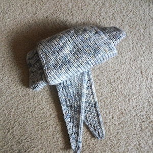 May include: A hand-knitted scarf in shades of blue, white, and gray. The scarf is made of a soft, textured yarn and features a ribbed knit pattern. The scarf is folded over on itself, with the ends hanging down.