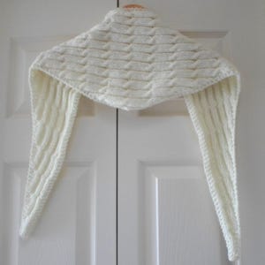 May include: A white knitted scarf with a cable knit pattern. The scarf is hanging on a hanger.