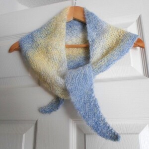 May include: A light blue and yellow knitted scarf with a gradient pattern. The scarf is hanging on a wooden hanger.