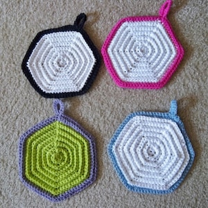 May include: Four crocheted hexagon pot holders with different colored borders. The pot holders are white with a black, pink, green, and blue border.