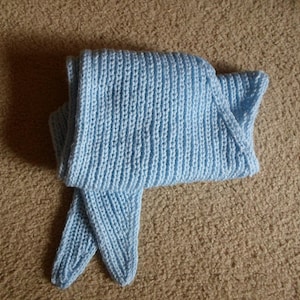 May include: A light blue knitted scarf. The scarf is folded and has a ribbed texture. The scarf is made of soft yarn and is a light shade of blue.