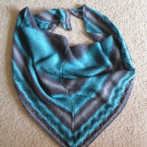 May include: A triangular shawl in shades of teal, gray, and silver. The knitted shawl features a striped pattern with a textured border. The soft, lightweight scarf is suitable for cool weather and adds a touch of elegance to any outfit.