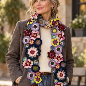 May include: A long crochet scarf featuring a vibrant array of multi-colored floral motifs in shades of red, yellow, blue, pink, and green. The scarf is constructed from various circular and flower-shaped yarn pieces joined together in a dense, textured pattern.