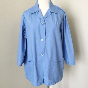 May include: A light blue button-down jacket featuring a classic collar, long sleeves, and two square patch pockets on the front. The garment is secured with three matching light blue buttons down the center front and includes vertical seam detailing.