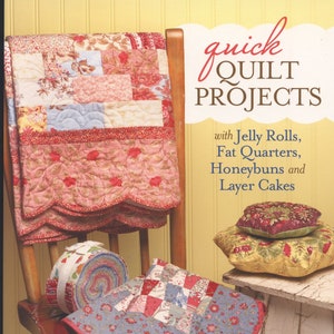 May include: A book cover titled "Quick Quilt Projects" with a quilt draped over a wooden chair. The quilt features various floral patterns in red, pink, and blue. Additional quilts and a roll of fabric are also visible.