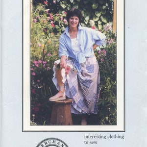 May include: A woman wearing a blue shirt and a patchwork skirt stands in a garden. The skirt is called "The Susannah Skirt" and is available from Merchant Rag, a company that sells interesting clothing to sew.