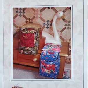 May include: A printed paper with the text "Quilter's Pincushion and Threadcatcher" and "The Pattern Basket". The image shows a pincushion and threadcatcher with floral and red fabric. A white swan figurine is also visible.