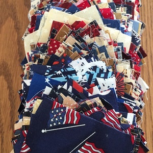 May include: A stack of fabric squares in red, white, and blue patriotic colors. The squares are made of different fabrics and have various patterns, including stars, stripes, and flags. The squares are arranged in a fan shape, with the bottom row of squares showing a pattern of American flags on a dark blue background.
