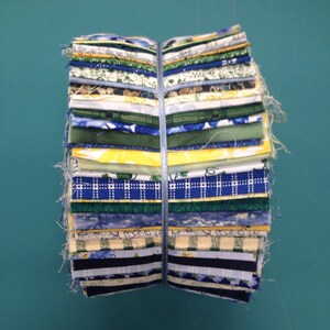 May include: A stack of fabric squares in various shades of blue, green, and yellow with floral and geometric patterns. The fabric is bundled together with a blue ribbon.