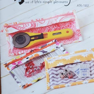 May include: Image of a sewing pattern titled "Bridget's Bagettes" by Atkinson Designs. The image shows three clear zippered pouches with sewing tools inside, including a rotary cutter, clips, bobbins, and needles.