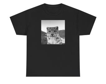 May include: Black t-shirt featuring a square, black and white image of a snow leopard. The image shows the leopard's face and upper body, set against a mountainous backdrop. The shirt is made of a soft, comfortable material.