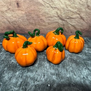 May include: Six small ceramic pumpkins with green stems. The pumpkins are orange and have a glossy finish.