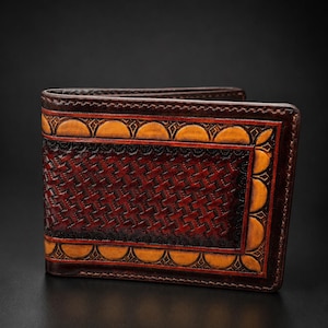 May include: A bi-fold wallet crafted from dark brown leather featuring a central rectangular panel with a deep red basket-weave texture. The border is decorated with a repeating pattern of golden-yellow semi-circles and dark brown stitching.