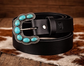 May include: A black belt featuring a silver-toned buckle adorned with six oval-shaped turquoise stones. The buckle has a scalloped edge and a polished metal finish. The belt strap is smooth black material with a single metal rivet and a loop.
