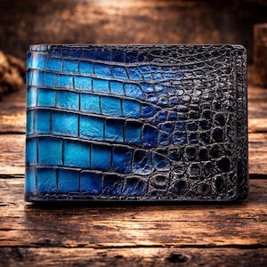 May include: A bi-fold wallet featuring a textured, embossed surface with a gradient color transition from bright blue on the left side to deep black on the right side. The material displays a distinct, repeating scale-like pattern throughout.