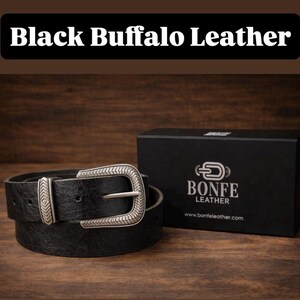 a black buffalo leather belt and its packaging box, both placed on a wooden surface.