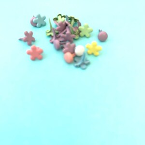 May include: A collection of pastel-colored metal flower-shaped brads. The brads are in shades of pink, green, yellow, and blue.