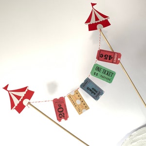 May include: Red and white circus tent toppers with red, green, blue, and yellow ticket banners that say "One Ticket" and "Adult one" hanging from a string.