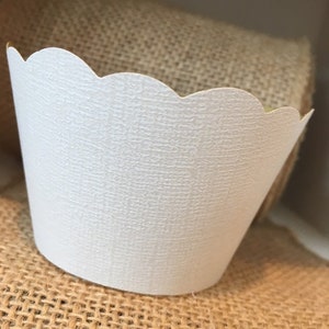 May include: White cupcake liners with a scalloped edge and a textured surface.
