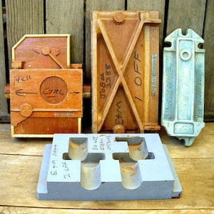 May include: Four wooden molds for casting metal parts. The molds are labeled with job numbers, part numbers, and instructions. One mold is blue and has the text "Do Not Clean Castings".