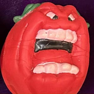 May include: Four novelty toys shaped like tomatoes and a cabbage, each with a unique facial expression. The toys are red, green, and white, with the text "ATTACK OF THE KILLER TOMATOES" in yellow.