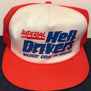Puede incluir: Una gorra de camionero blanca y roja con un logotipo azul y rojo que dice "Imperial Hell Drivers Wildest Show on Wheels".
