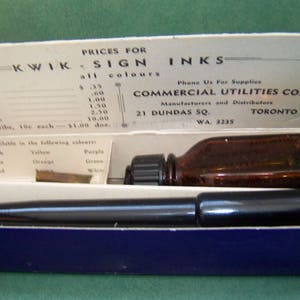 Puede incluir: Una caja azul con una botella de vidrio marrón de tinta y una pluma negra. La caja tiene una etiqueta que dice "Kwik Sign Inks" y "Commercial Utilities Co. Manufacturers and Distributors Toronto 21 Dundas Sq. WA. 3235".
