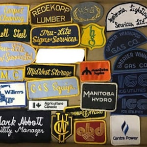 Może przedstawiać: Kolekcja vintage haftowanych naszywek z różnymi logotypami firm, w tym "Redekopp Lumber", "Tru-Lite Signs-Services", "Ambrose Lighting Services Ltd.", "Greater Winnipeg Gas Co.", "Midwest Storage", "C.G.S. Equip", "Manitoba Hydro", "Winnipeg Hydro", "IGG Utilities" i "Centra Power".