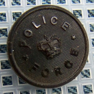 Puede incluir: Un botón de plástico negro con las palabras "POLICE" y "BORO" alrededor de un diseño de corona.