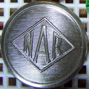 May include: A silver metal button with a diamond-shaped design. The letters "NAR" are embossed in the centre of the diamond.