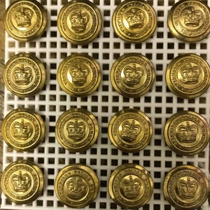 May include: A collection of sixteen gold-colored buttons, each featuring a detailed crown design at the center. The buttons are arranged in a grid pattern on a white, square-holed surface. The text "TORONTO POLICE FORCE" is visible on each button.