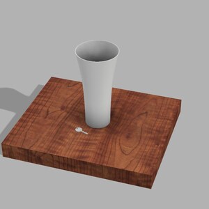 May include: A white ceramic vase sits on a wooden base with a small white key lying next to it.