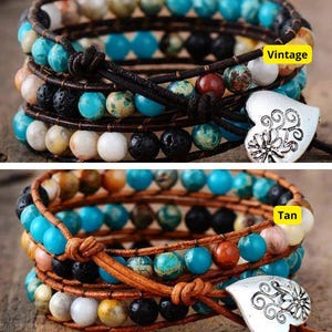Op de afbeelding: Twee meerstrengs wikkelarmbanden met turquoise, bruine en zwarte kralen. De armbanden hebben een zilveren hartvormige hanger met een bloemenmotief. De bovenste armband is geëtiketteerd met "Vintage" en de onderste met "Tan".