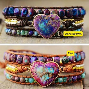 May include: Two multi-layered leather wrap bracelets with a heart-shaped stone pendant. The top bracelet has a dark brown leather strap and the bottom bracelet has a tan leather strap. Both bracelets feature a variety of colorful stones and beads.