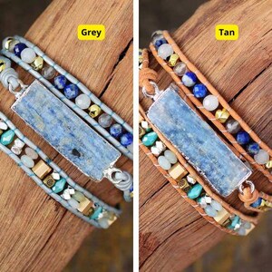 Puede incluir: Dos pulseras de capas con detalles de piedras azules y una piedra rectangular azul en el centro. La pulsera de la izquierda tiene una base de cuero gris y la pulsera de la derecha tiene una base de cuero marrón. El texto "Gris" está sobre la pulsera de la izquierda y el texto "Tan" está sobre la pulsera de la derecha.