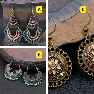 以下が含まれることがあります： 複雑なデザインのぶら下がり式のイヤリングが3組。最初のペアは、多色のデザインの涙滴型のセンターストーンが特徴です。2番目のペアは、花柄の丸いセンターストーンが特徴です。3番目のペアは、多色のデザインの丸いセンターストーンが特徴です。