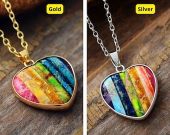 Könnte beinhalten: Eine Halskette mit einem regenbogenfarbenen herzförmigen Anhänger mit einer goldenen oder silbernen Kette. Der Anhänger ist aus buntem Stein mit einem gestreiften Muster.