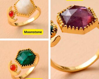 May include: Four gold rings with different colored gemstones. The rings feature a crescent moon design with a small red gemstone on the side. The gemstones are amethyst, moonstone, malachite, and a white stone. The text "Amethyst", "Moonstone", "Malachite" is visible below each ring.