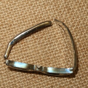May include: A silver metal ring with a gap in the band. The ring is lying on a brown burlap surface.