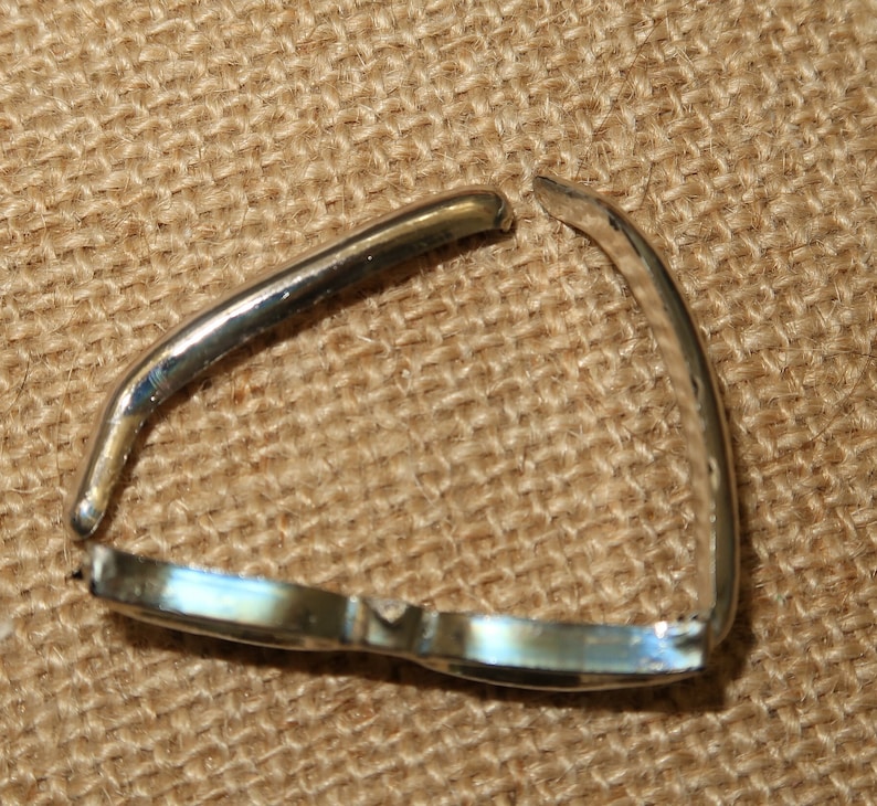 May include: A silver metal ring with a gap in the band. The ring is lying on a brown burlap surface.