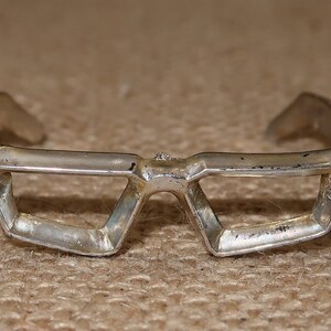 May include: A silver geometric bracelet with a unique, angular design. The bracelet is open and has a rounded edge on each side.