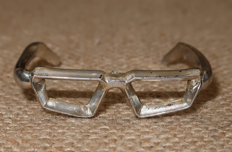 May include: A silver geometric bracelet with a unique, angular design. The bracelet is open and has a rounded edge on each side.