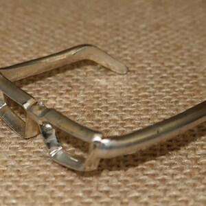 May include: Silver-toned metal glasses with a unique, angular design. The glasses have a wide, open frame and a slightly curved bridge.