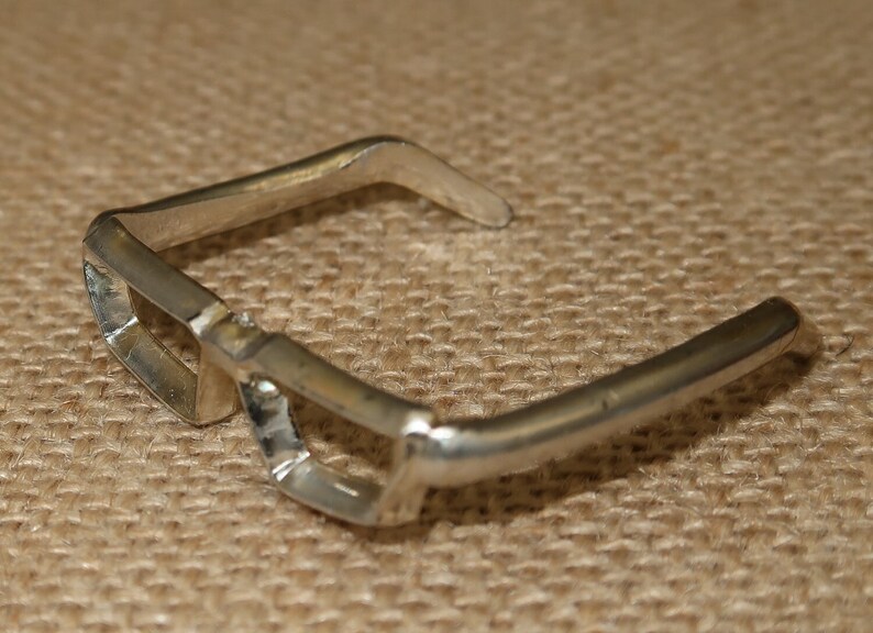 May include: Silver-toned metal glasses with a unique, angular design. The glasses have a wide, open frame and a slightly curved bridge.