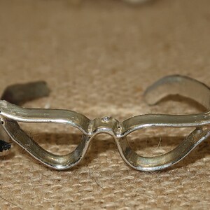 May include: Silver-toned cat-eye glasses with a simple design. The glasses are made of metal and have a smooth finish.
