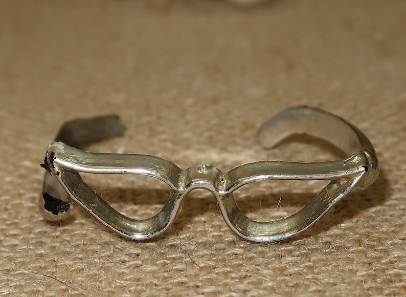 May include: Silver-toned cat-eye glasses with a simple design. The glasses are made of metal and have a smooth finish.