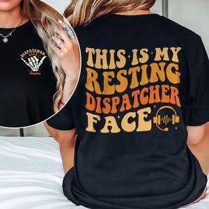 May include: Black t-shirt with the text "THIS IS MY RESTING DISPATCHER FACE" in orange and yellow retro font. The front of the shirt has a small design with the words "DISPATCHER LIFE" and a skeleton hand. A headset graphic is on the back.